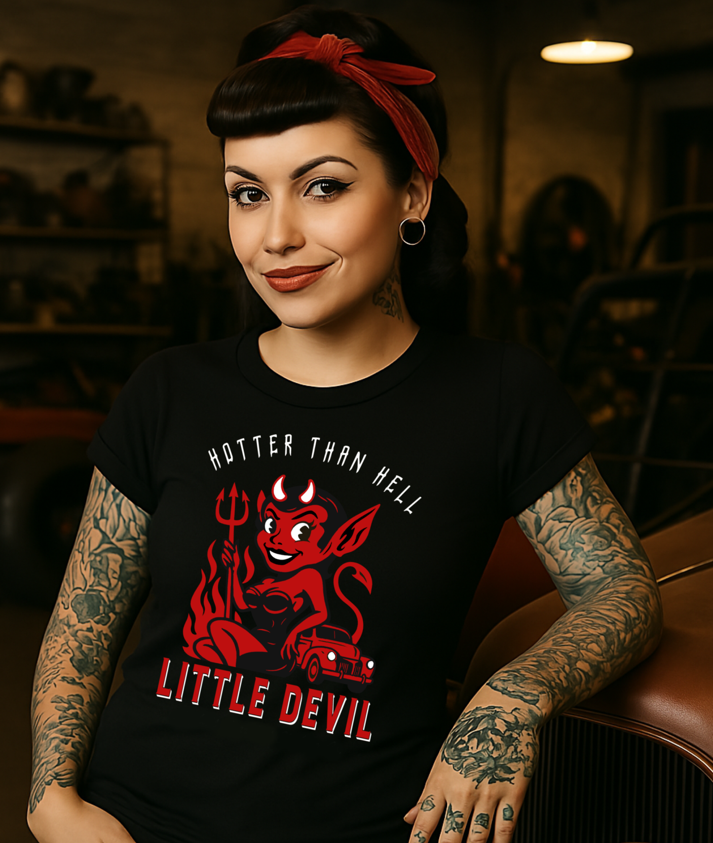 
                  
                    Black ‘Little She Devil’ women’s soft-style crew tee by Asphalt Anarchist Clothing Co., featuring vintage-inspired hot rod artwork and retro pin-up flair, worn by a cute tattooed rockabilly woman hanging out at the hot rod shop; image is AI-generated
                  
                