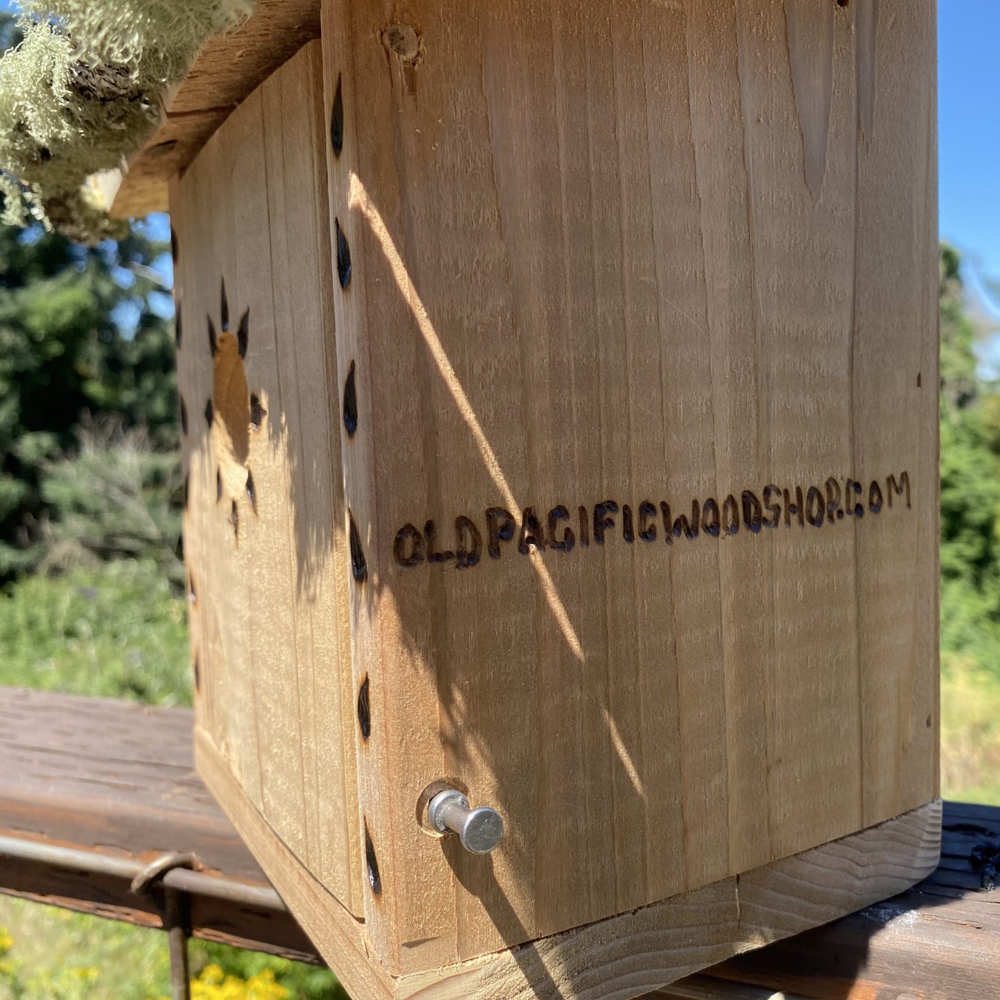 
                  
                    Branding Image. Wooden birdhouse with natural elements on a wooden post against a blue sky and green trees background. Sparrow Shack Birdhouse by Old Pacific Woodshop HANDMADE COUNTRY WOODWORK 
                  
                